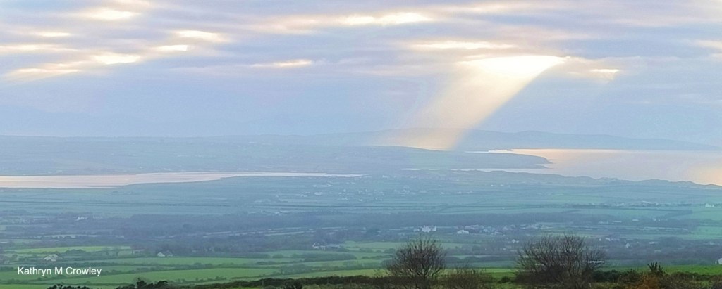 My photo of light coming through clouds over fields and a river in the valley below.
