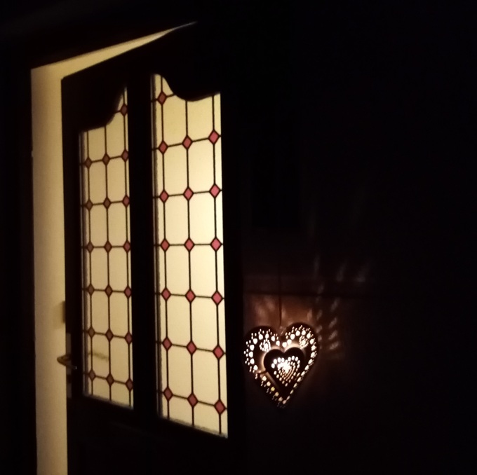 Night time photo of a door open with lights on inside the house. On the front facade is a heart-shaped light.